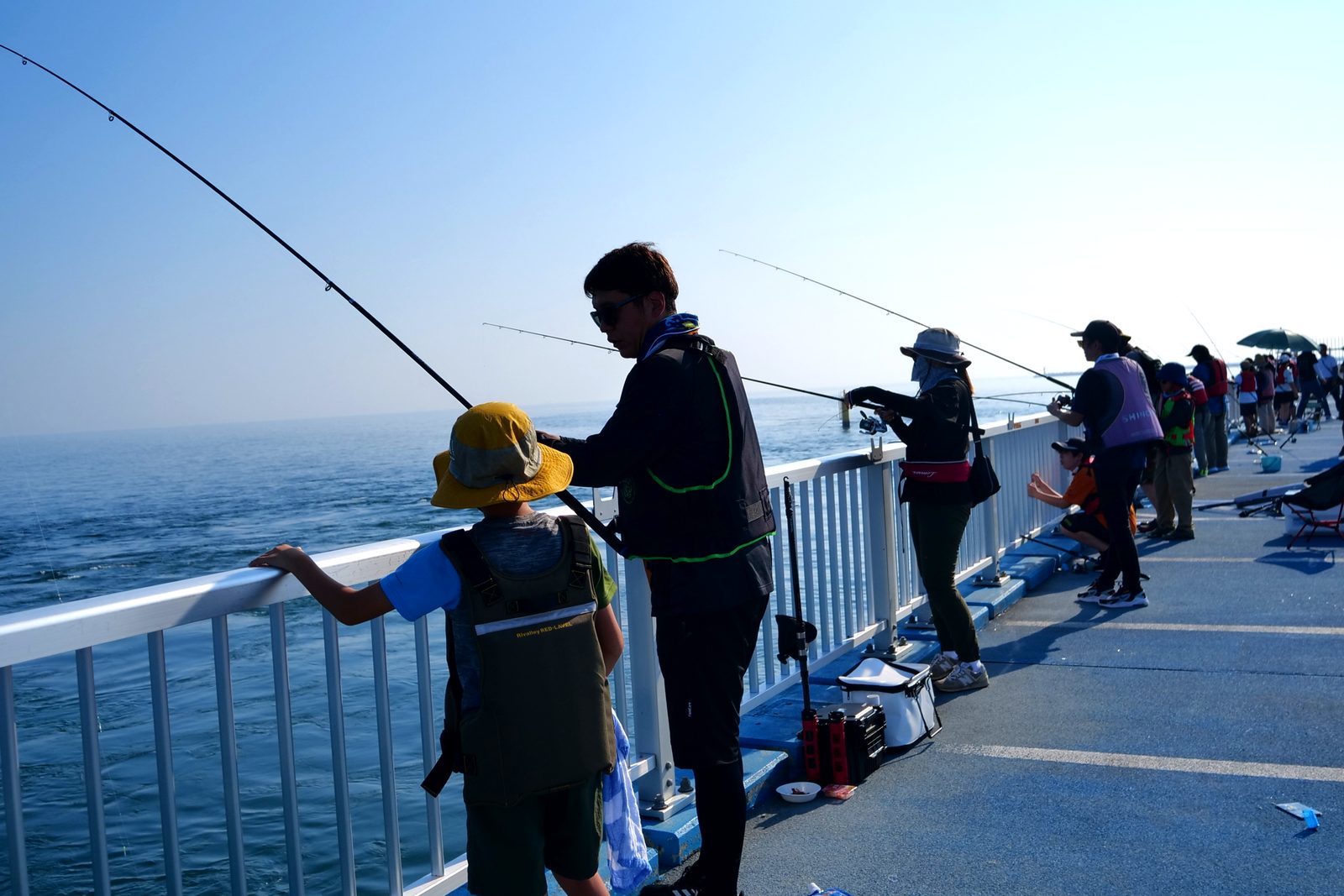 海釣り公園のデッキに並んで竿を出す釣り人たち。手前では子どもが手すりから海をのぞいている