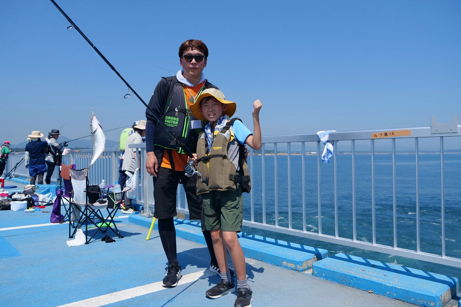 デッキで、釣れた魚を掲げる男性とガッツポーズをする子ども