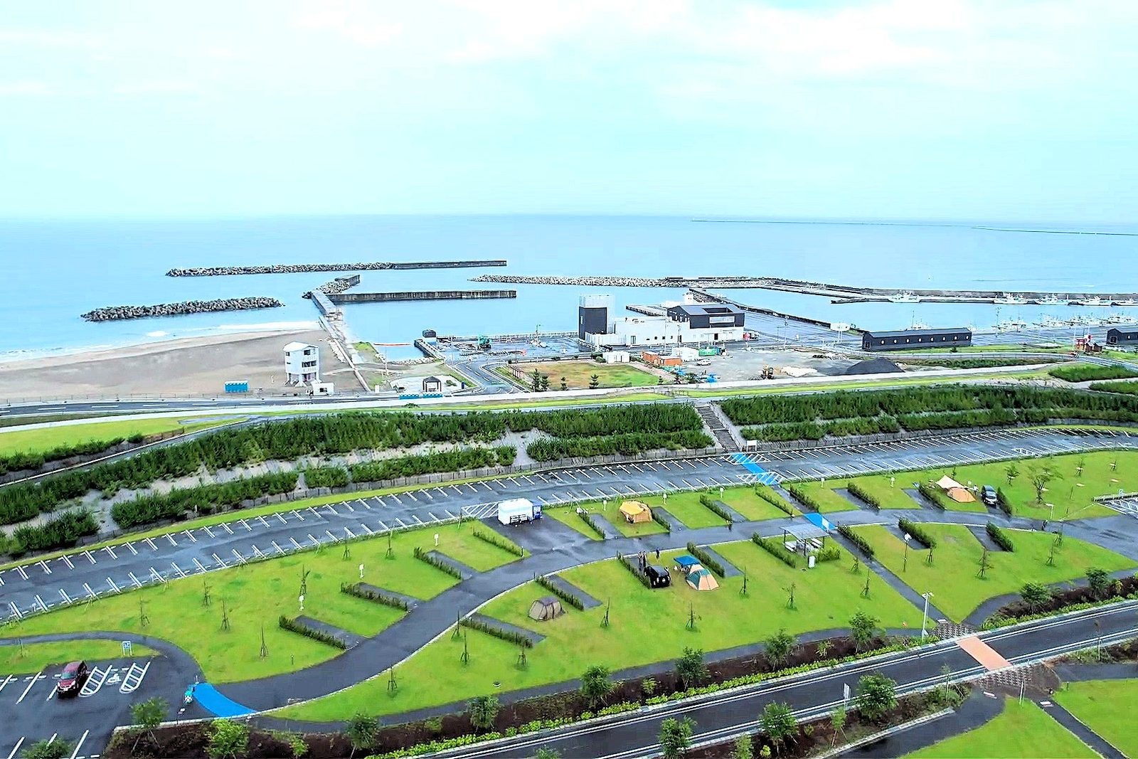 上空から見た釣師防災緑地公園。芝生とテント、その先に相馬港と太平洋が広がる