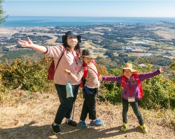 山頂で両手を広げる親子の参加者。背景に新地町の平野と太平洋